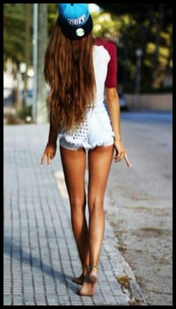 Woman with long hair and a baseball cap walking on a street