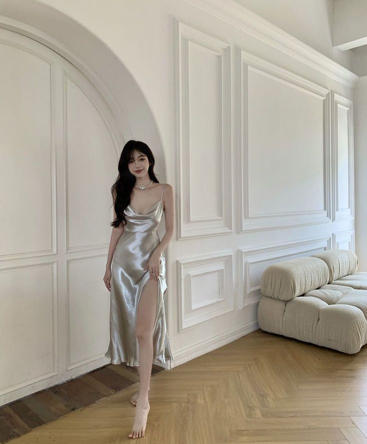 Woman in a silver high-slit dress standing barefoot indoors