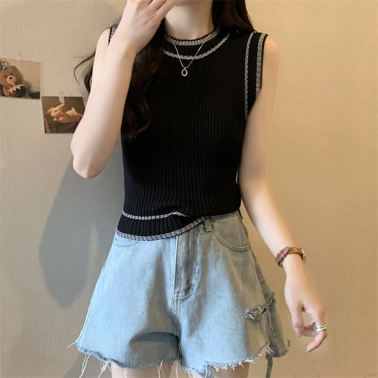 Person in a black sleeveless top and denim shorts with a necklace and watch