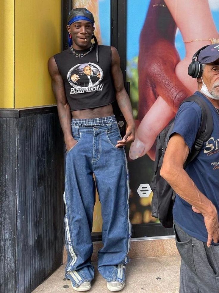 Person in a crop top and baggy jeans leaning against a wall outdoors