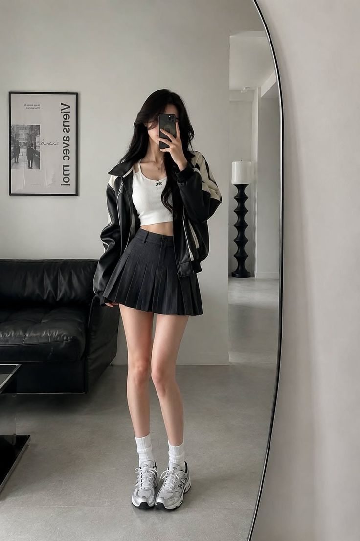 Woman in a crop top and pleated skirt taking a mirror selfie indoors