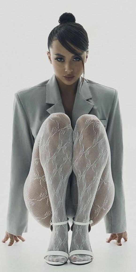 Woman in a gray blazer and white fishnet stockings squatting in a studio