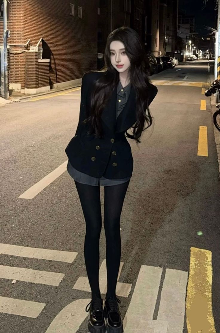 Woman with long dark hair wearing a blazer and shorts on a street at night