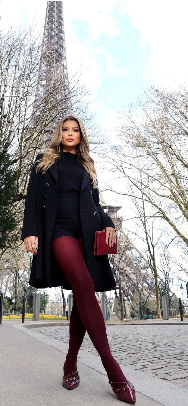 Woman in a black coat and red tights posing outdoors with the Eiffel Tower in the background