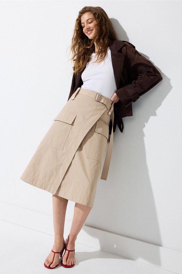 Woman with long wavy hair wearing a beige skirt and brown jacket