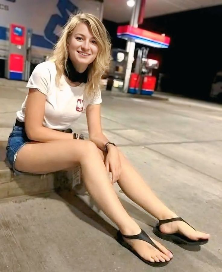 Blonde woman in a white t-shirt and denim shorts sitting at a gas station at night