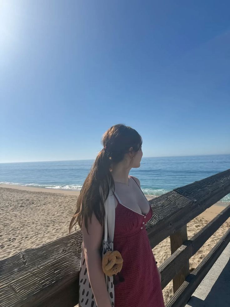 Woman in a red dress with a ponytail looking out at the ocean from a pier