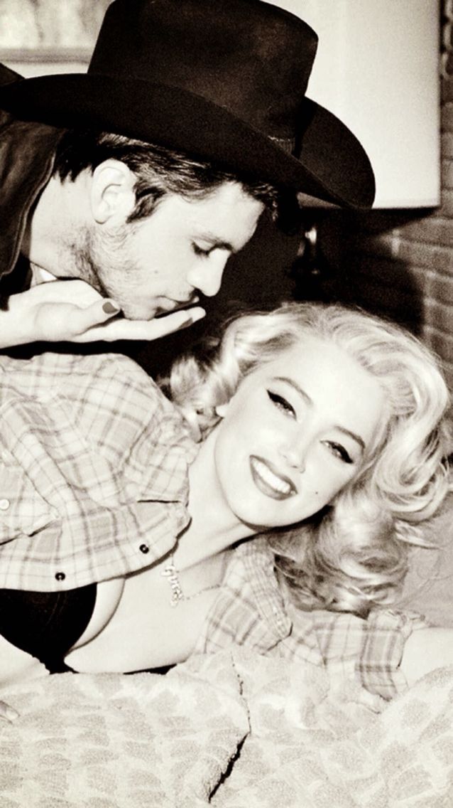 Man in a cowboy hat kissing a woman with blonde curly hair in a plaid shirt
