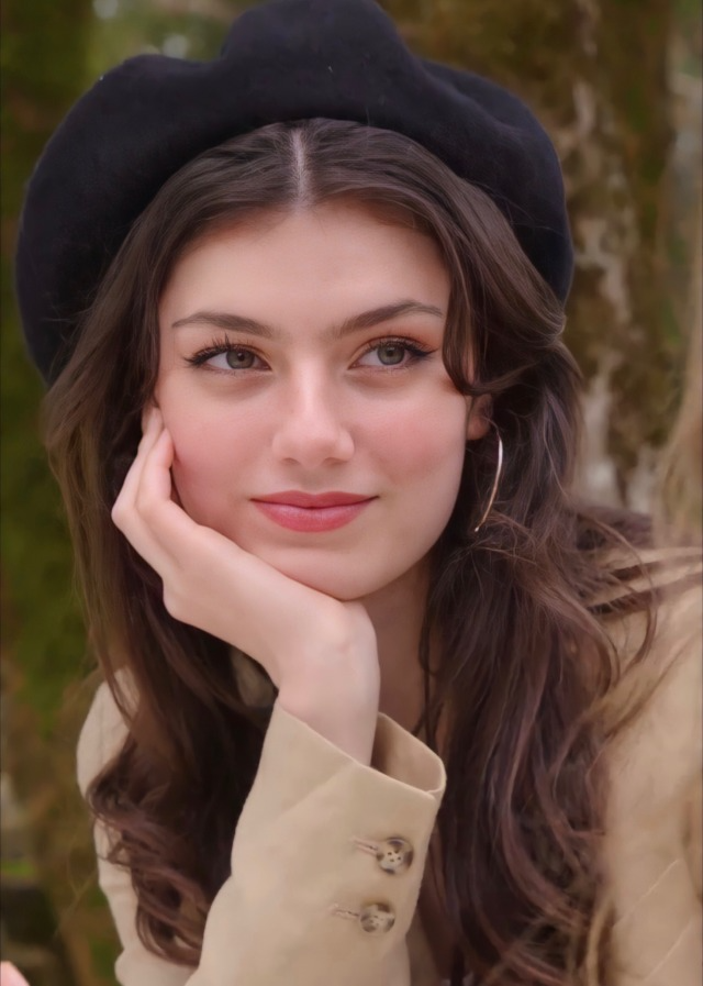 Woman with long wavy hair and a black beret, resting her chin on her hand