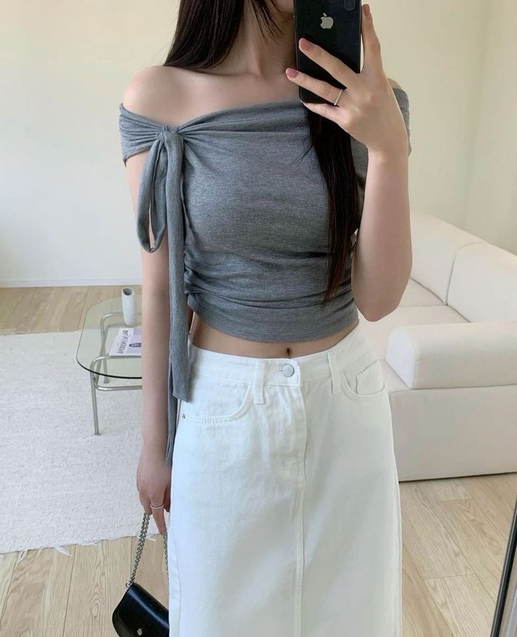 Woman in an off-shoulder crop top and white skirt taking a mirror selfie