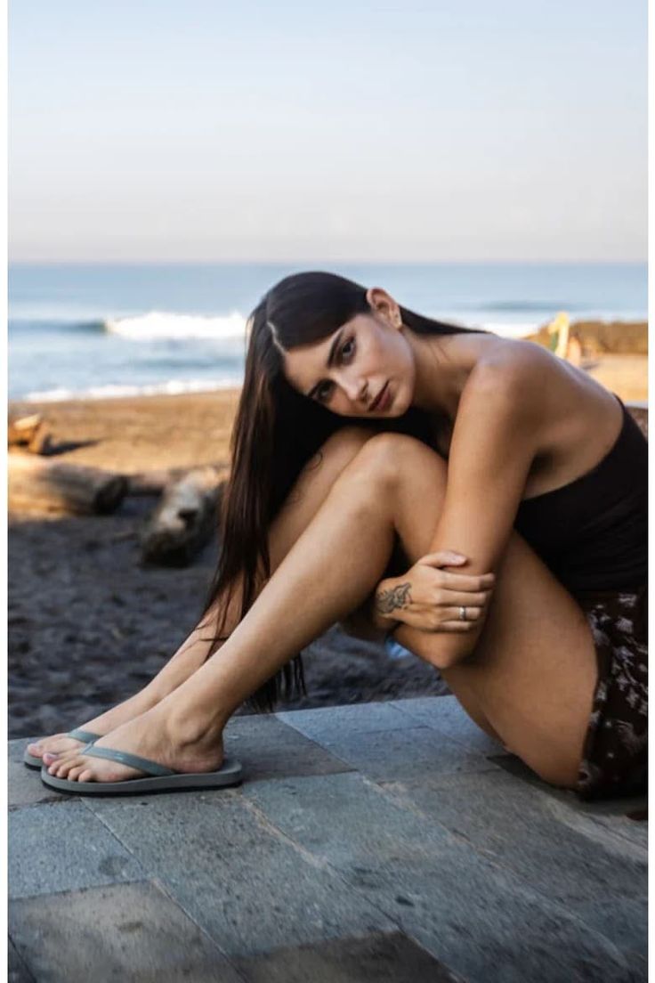 Woman with long dark hair sitting on a stone ledge at the beach