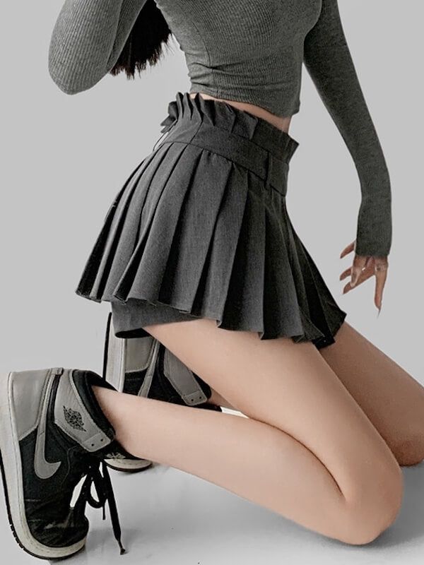 Person in a gray crop top and pleated skirt kneeling in a studio