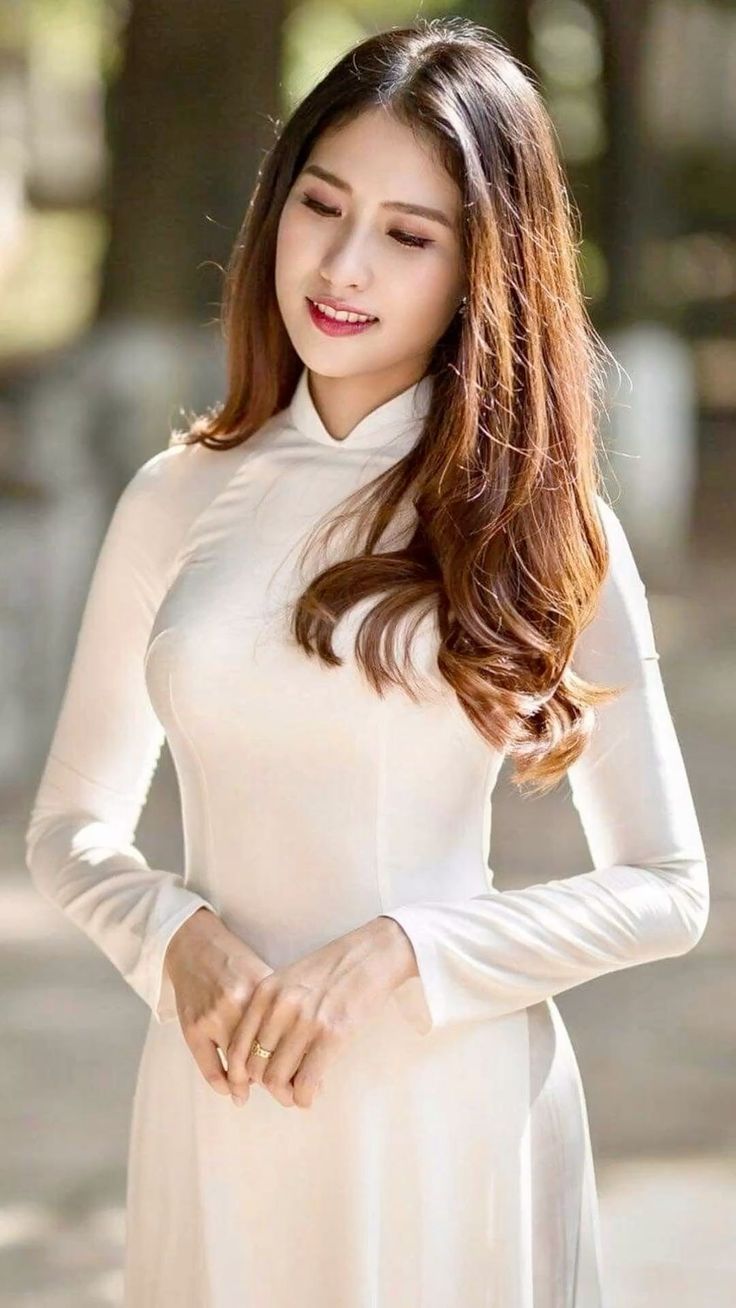 Woman with long brown hair wearing a white dress outdoors with soft lighting