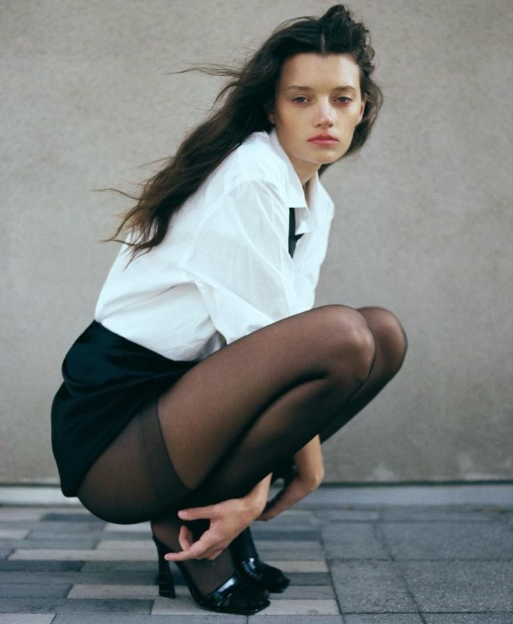 Woman in a white shirt and black tights squatting outdoors