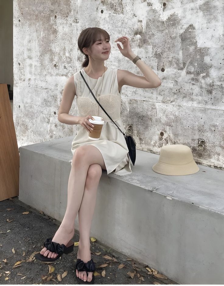 Woman in a sleeveless dress sitting on a concrete bench with a coffee cup