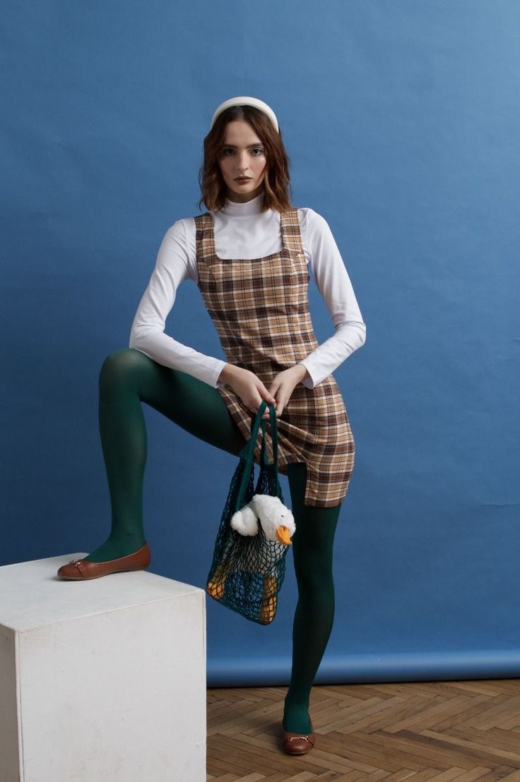 Woman in a plaid dress and green tights holding a mesh bag with a duck toy