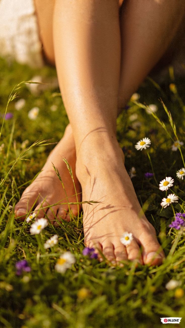 Bare feet crossed in green grass with small white and purple flowers