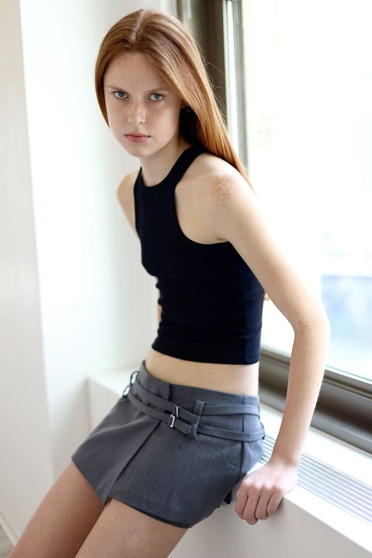 Young woman with red hair and freckles wearing a black tank top and mini skirt