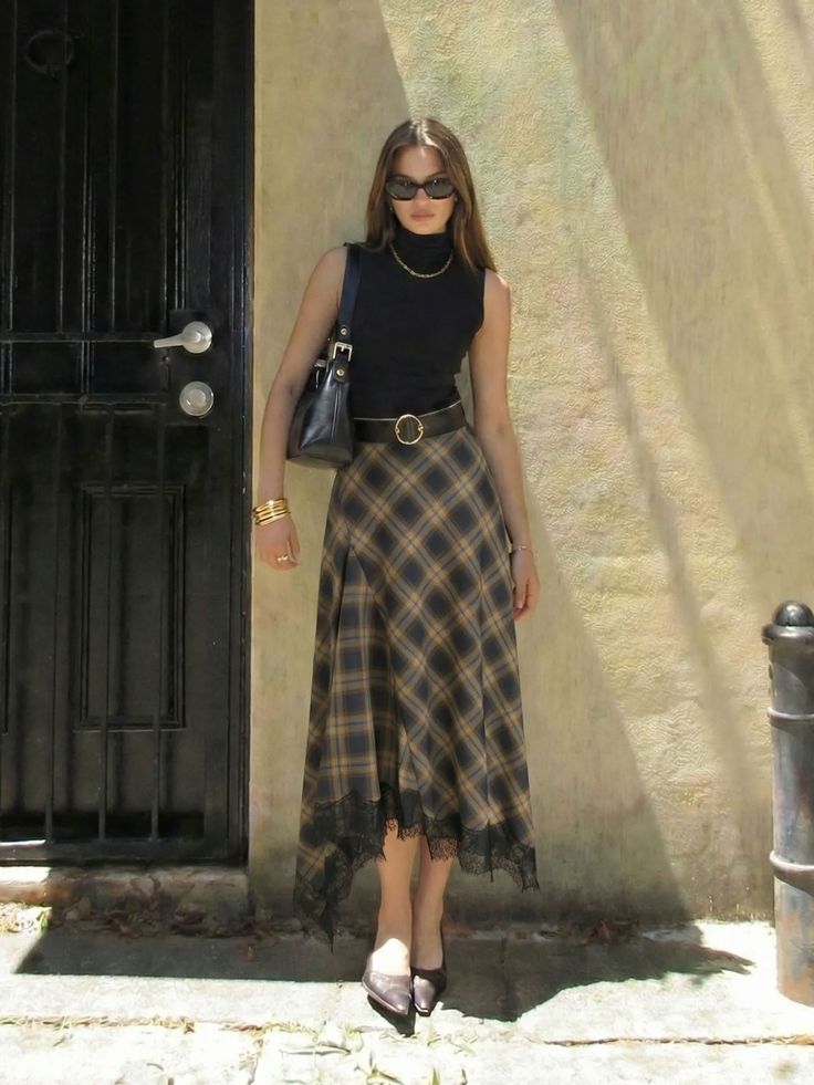 Woman in a black top and plaid skirt with sunglasses standing outdoors