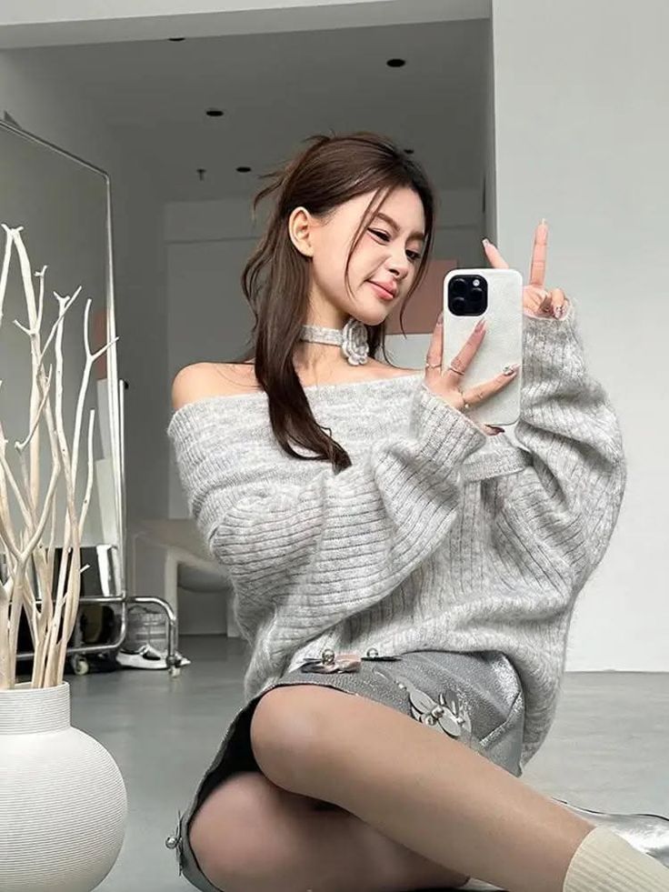 Woman in an off-shoulder sweater and silver shorts taking a selfie