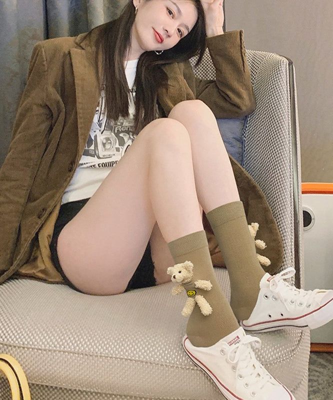 Woman with long hair wearing a brown jacket and teddy bear socks, sitting indoors