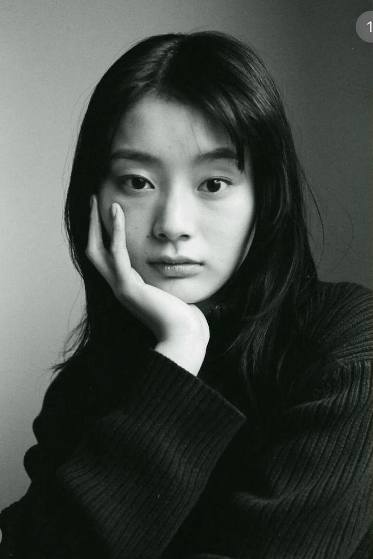 Woman with long black hair in a black sweater, resting her chin on her hand