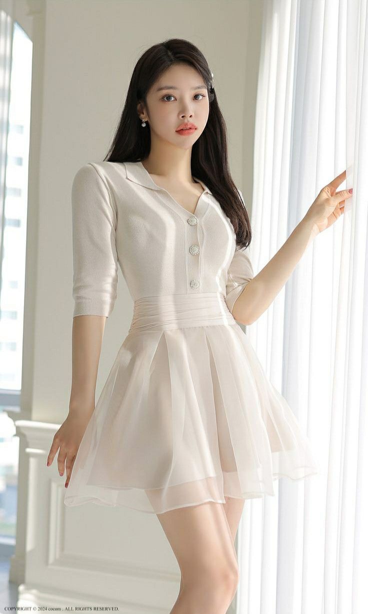 Woman in a white dress with a pleated skirt standing indoors