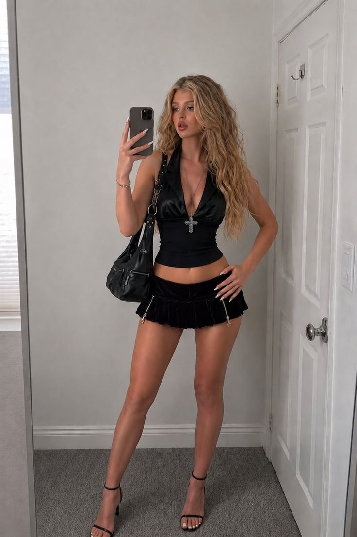 Woman in a black halter top and mini skirt taking a mirror selfie