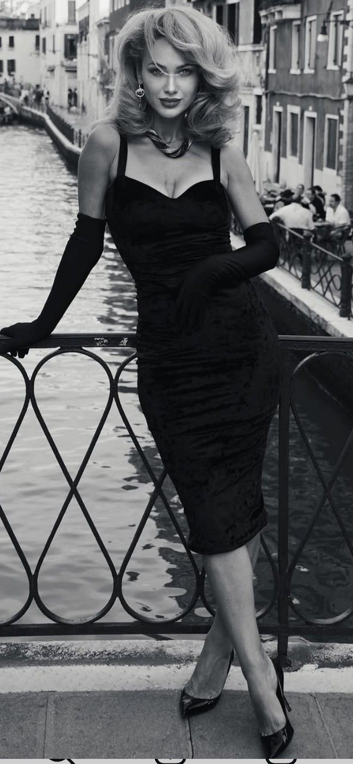 Woman in a black dress and long gloves posing by a canal