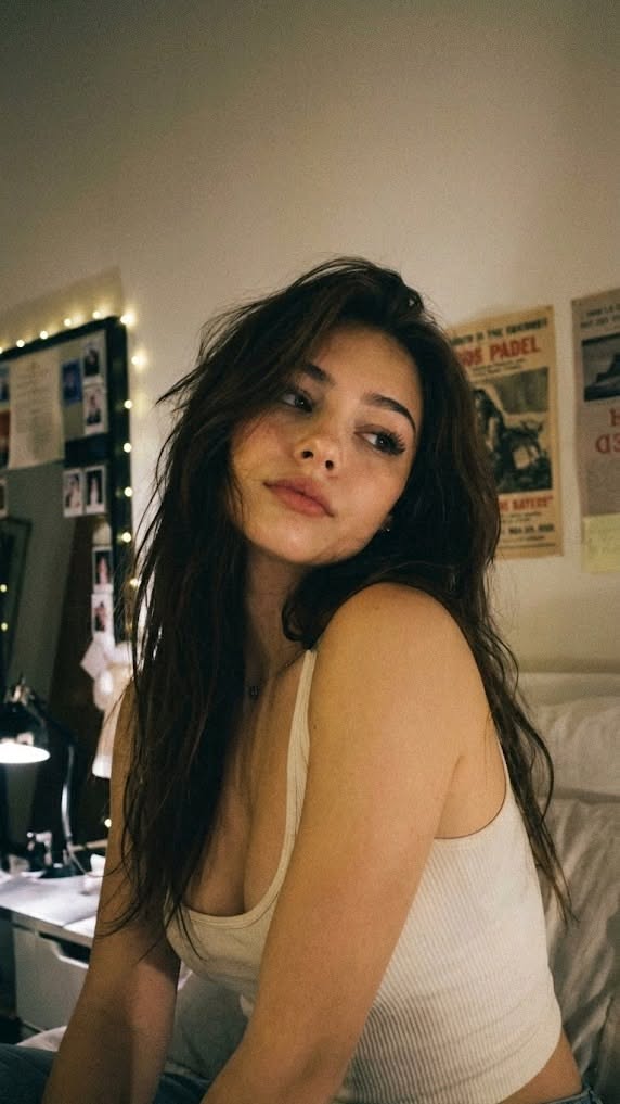 Woman with long hair in a white tank top indoors with soft lighting