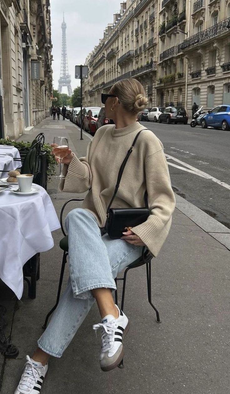 Woman with a hair bun and sunglasses sitting at an outdoor cafe with the Eiffel Tower in the background