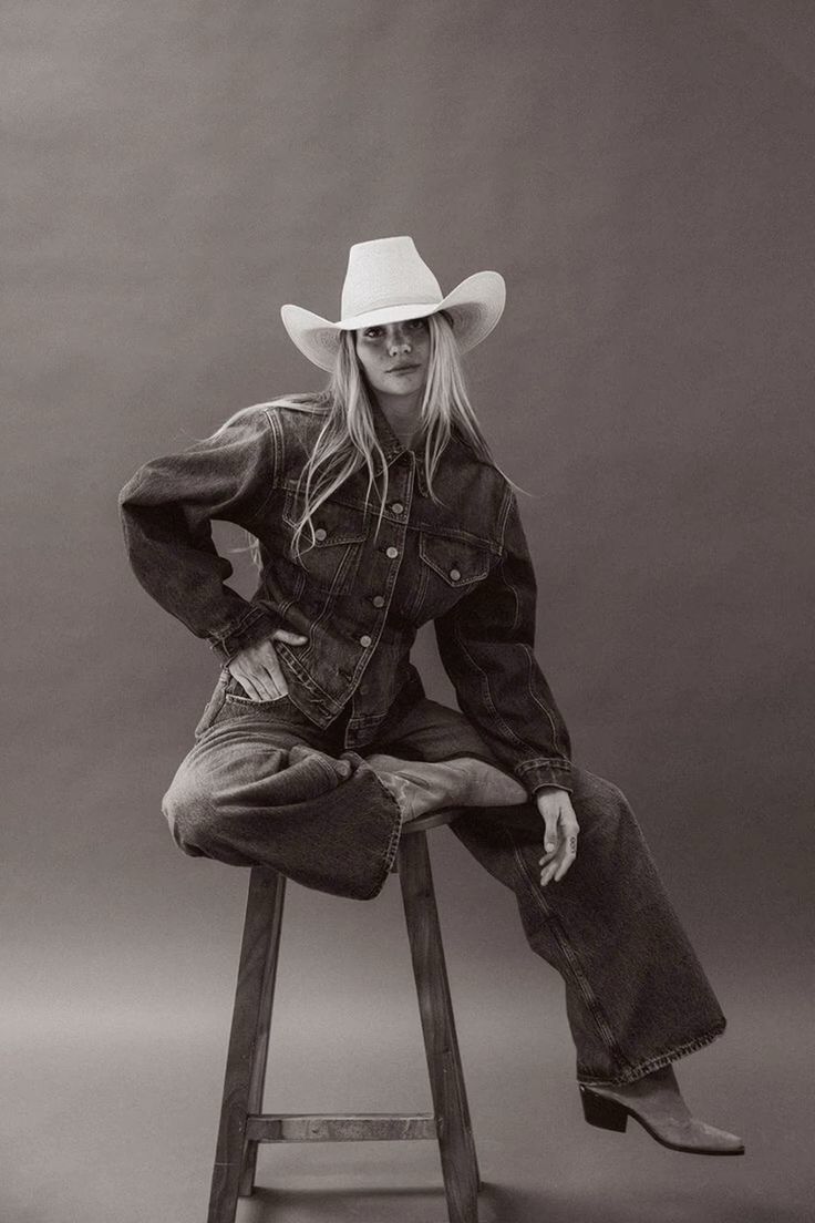 Woman in a cowboy hat and denim outfit sitting on a stool in a studio