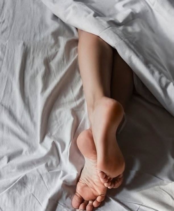Bare feet peeking out from under white sheets in a bed