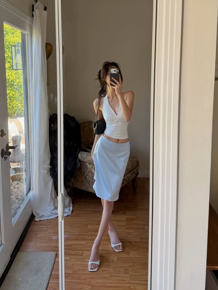 Woman in a white halter top and light blue skirt taking a mirror selfie