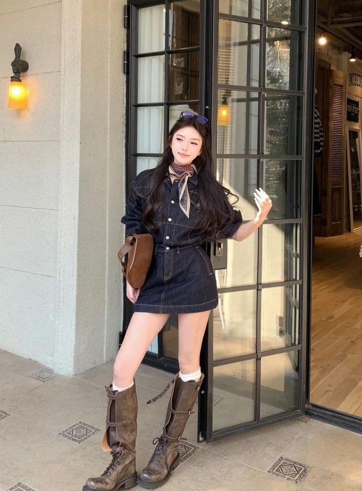 Woman in a denim dress and brown boots standing outside a building