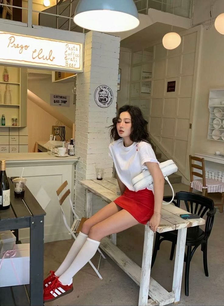 Woman with long dark hair in a red skirt and white t-shirt sitting on a table in a cafe