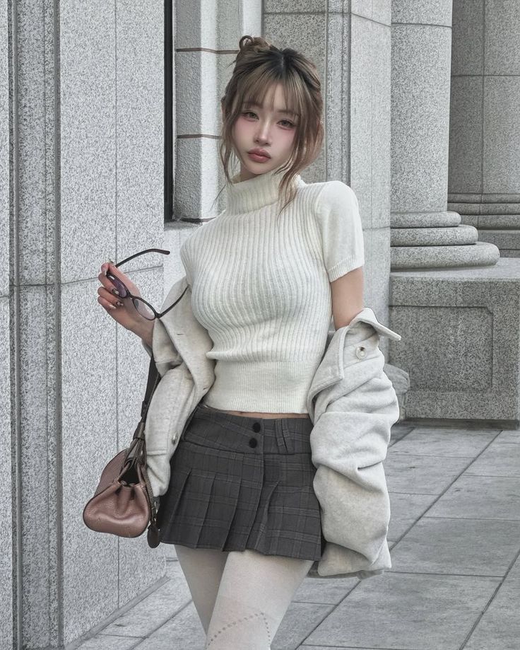 Woman in a white turtleneck and pleated skirt holding glasses outdoors