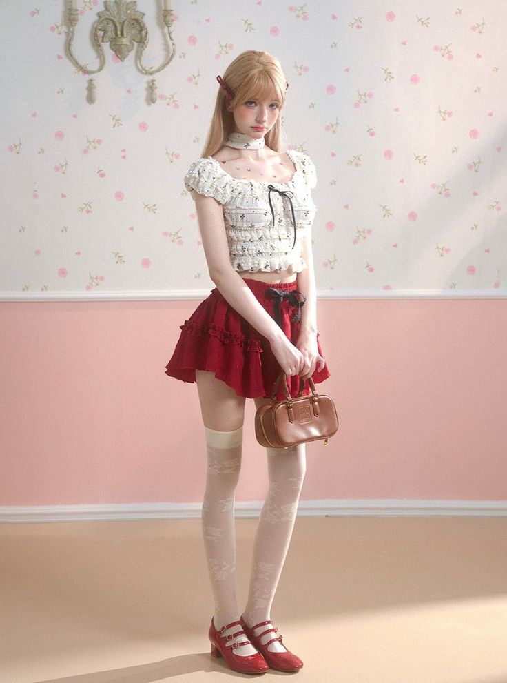 Blonde woman in a red skirt and crop top holding a small handbag indoors