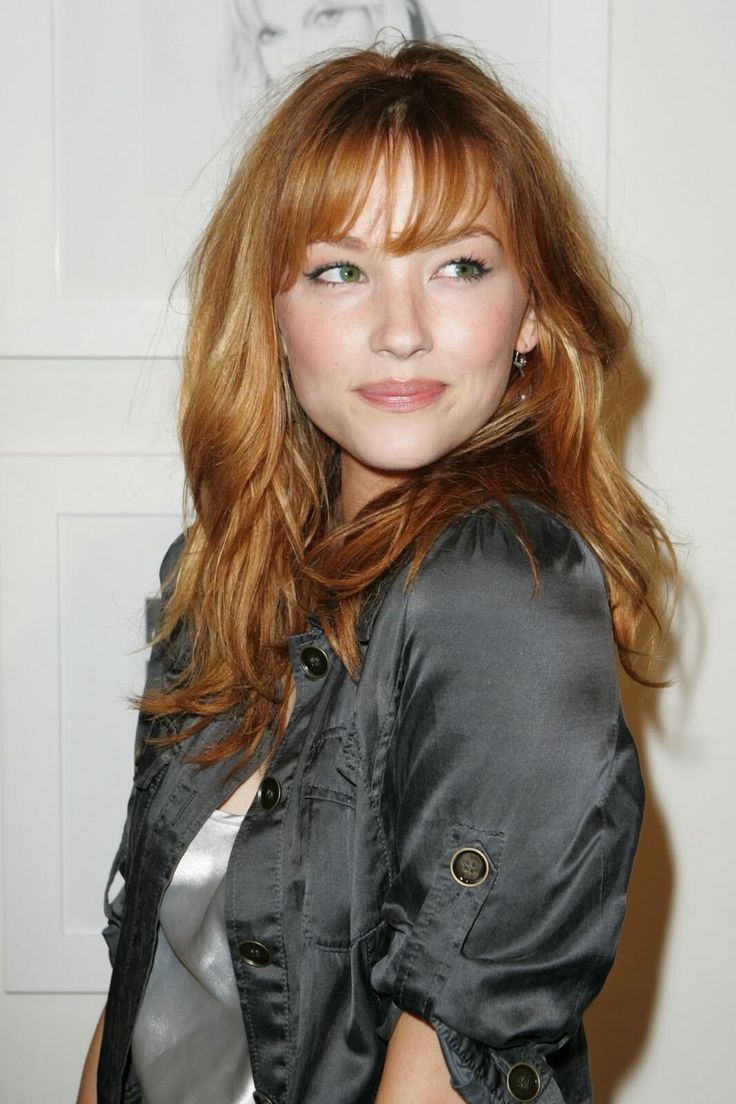 Woman with red hair and green eyes wearing a grey jacket indoors