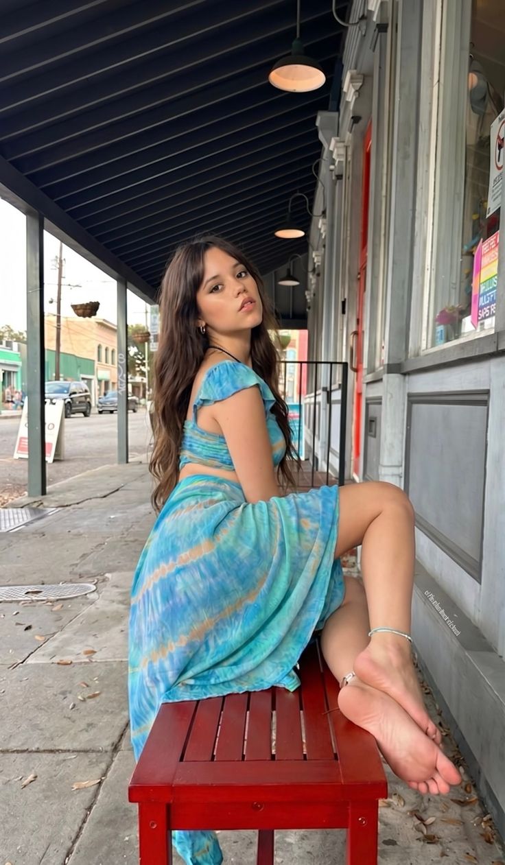 Woman with long hair in a tie-dye dress sitting on a red bench outdoors
