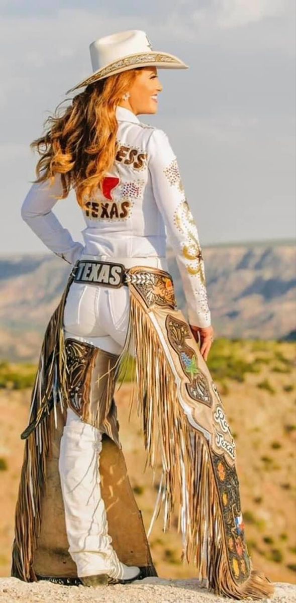 Woman in a white cowgirl outfit with chaps and a hat in a desert landscape