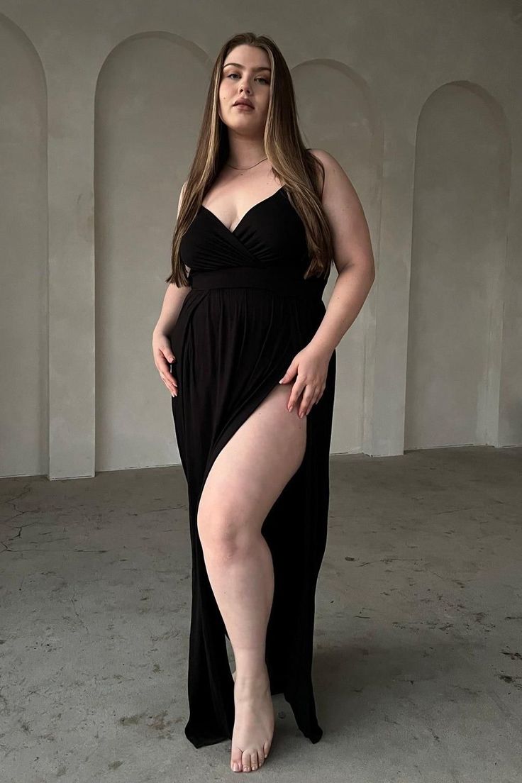 Woman in a black dress with a high slit posing indoors