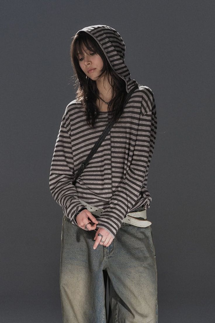 Person in a striped hoodie and baggy jeans looking down against a dark background
