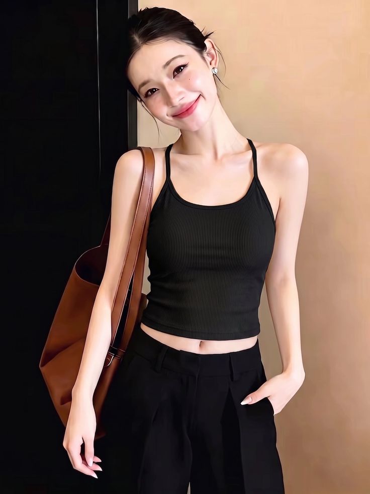 Woman in a black tank top and black pants with a brown bag, smiling indoors