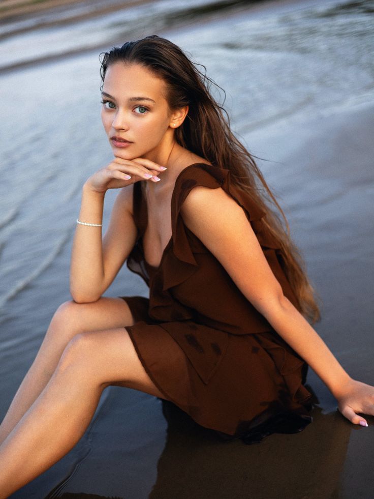 Woman with wet long hair and a brown dress sitting on a beach