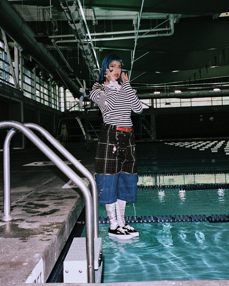 Person with blue hair and striped shirt standing in an indoor pool