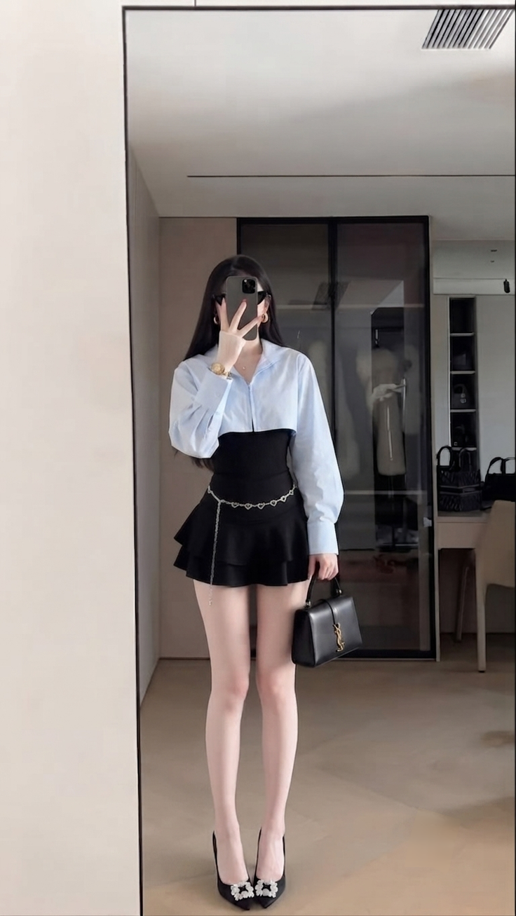 Woman in a light blue shirt and black mini skirt taking a mirror selfie