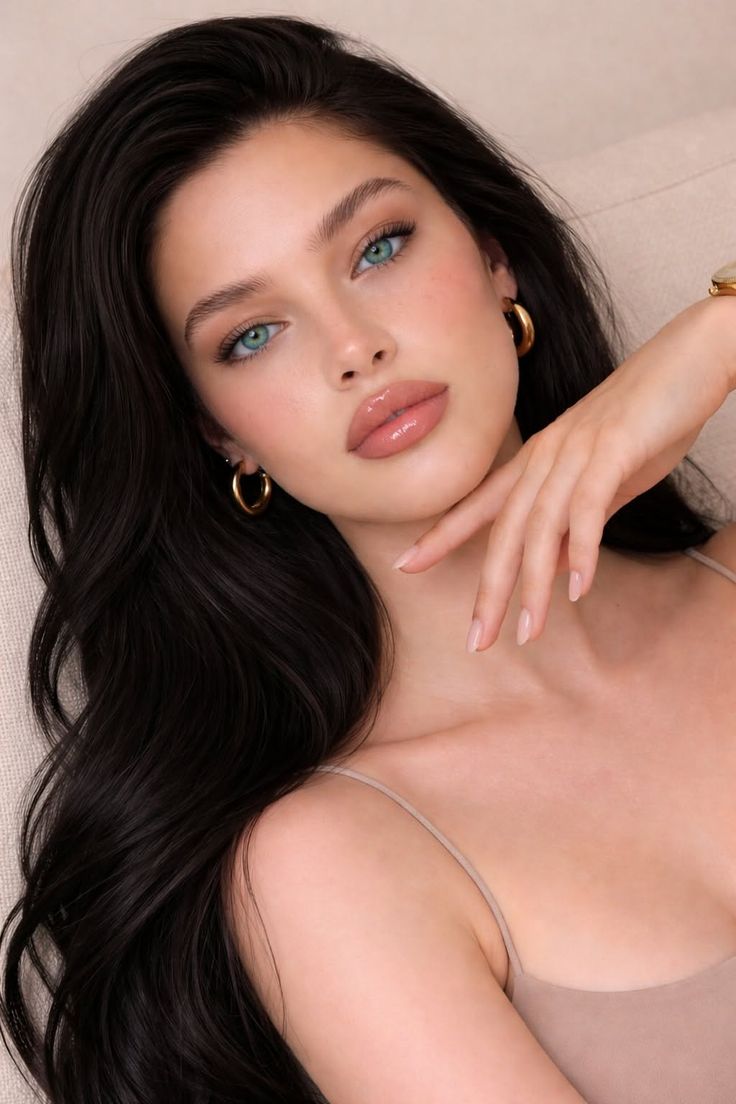 Woman with long black hair and blue eyes wearing a beige top