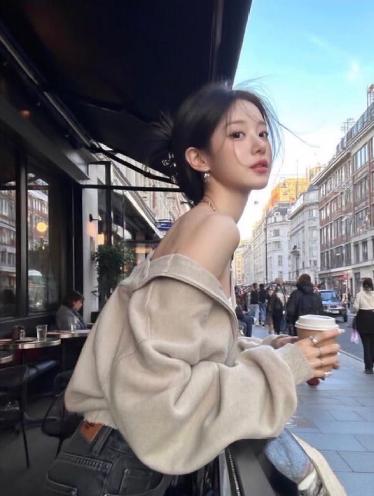 Woman in an off-shoulder top holding a coffee cup on a city street