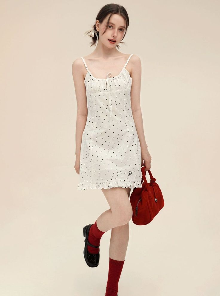Woman in a white polka dot dress with red socks and a red handbag posing in a studio